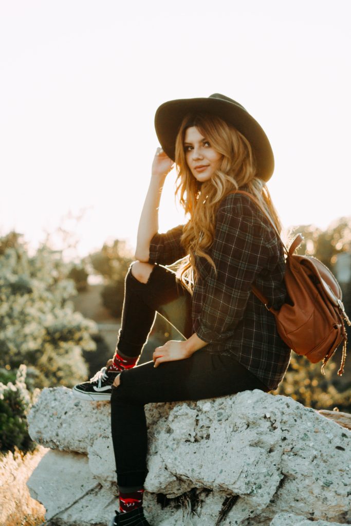 woman wearing a hat and backpack, sitting on a rock 