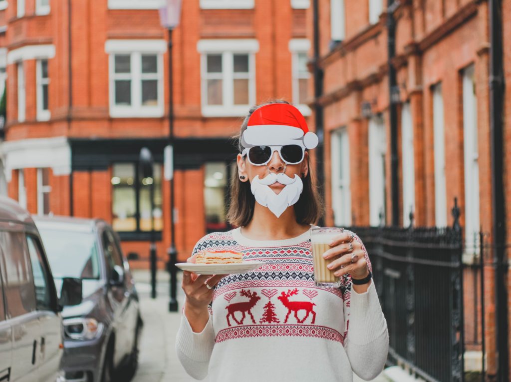 woman wearing a Christmas sweater, santa hat and has a fake Santa beard